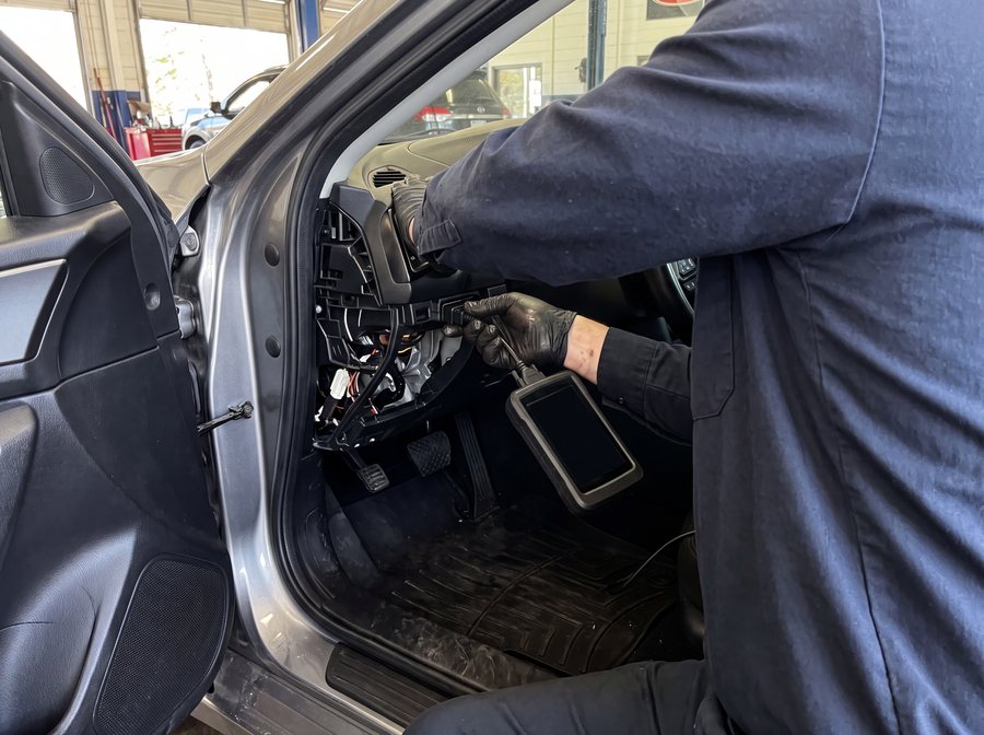 A mechanic's gloved hands connecting a diagnostic scan tool to a car's under-dash port